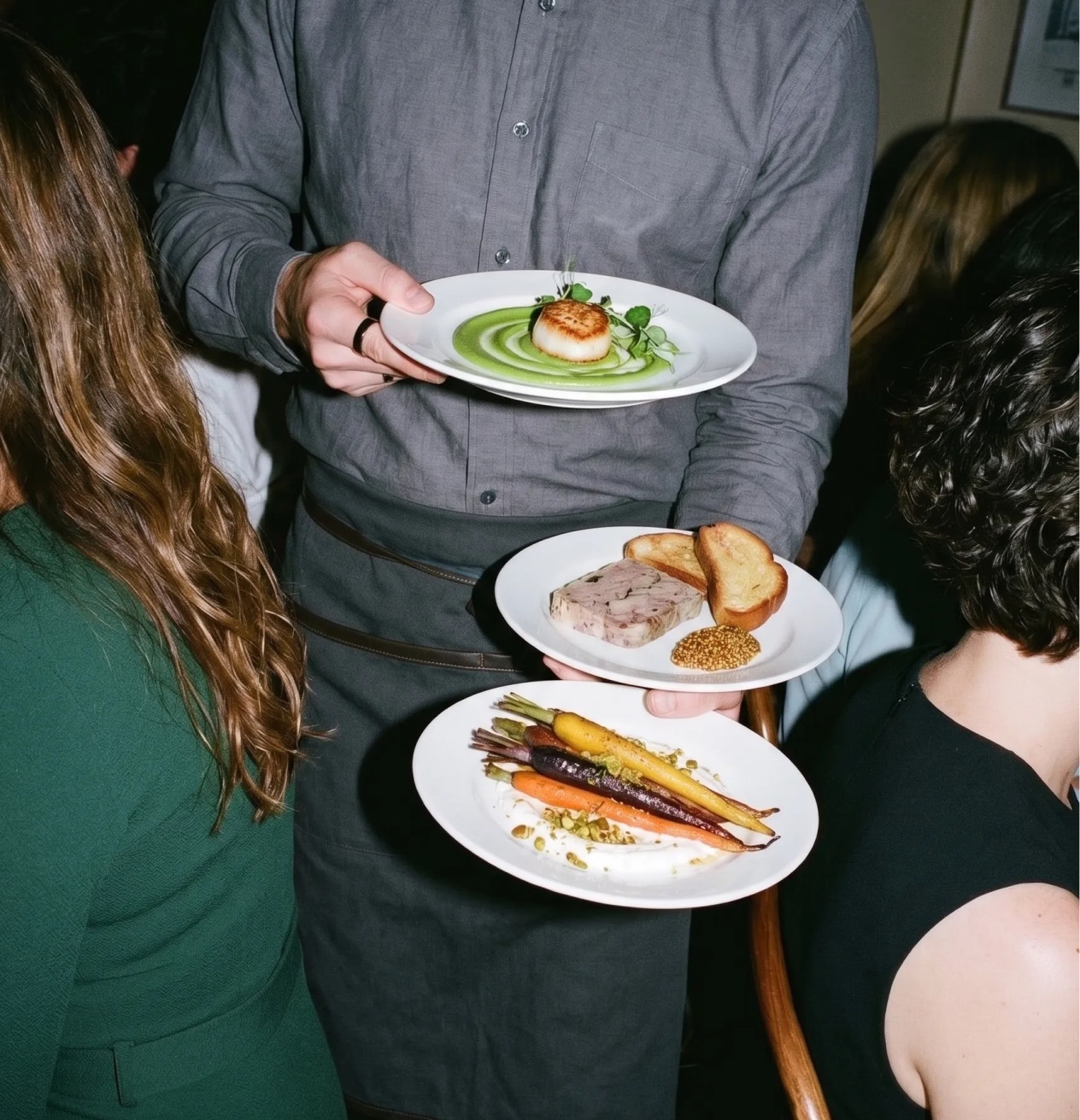 A server carrying three plated courses through a crowd at an event